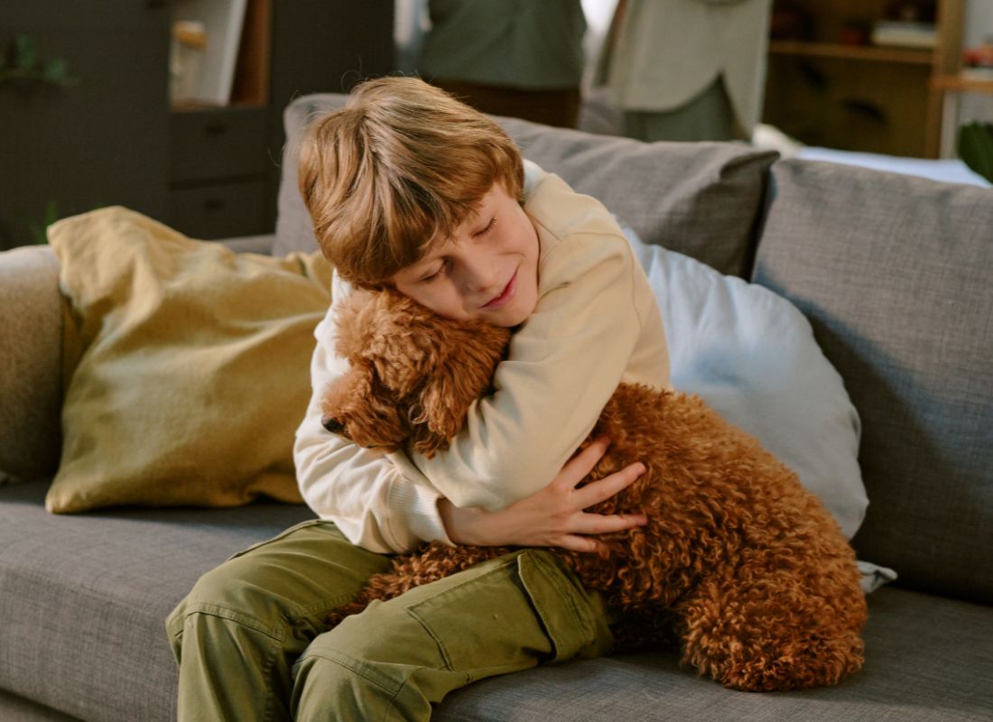 Boy hugging brown poodle.